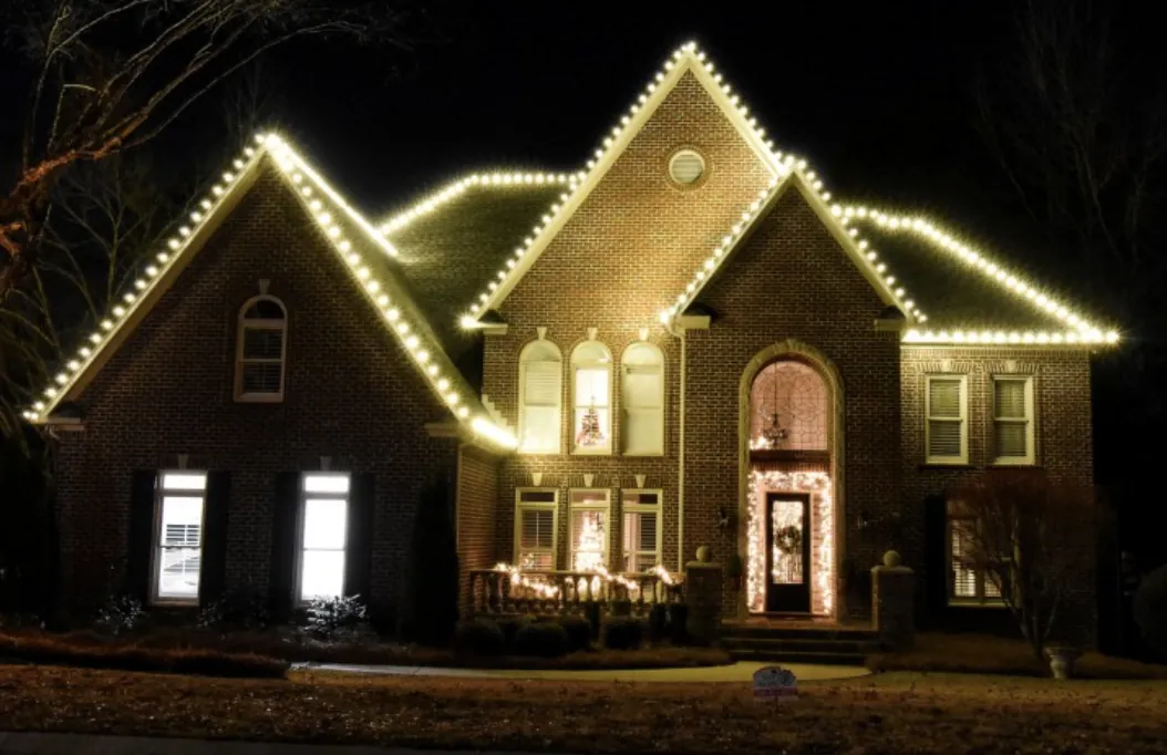 White roofline lights on a brick home with a tall arched front entry at night.
