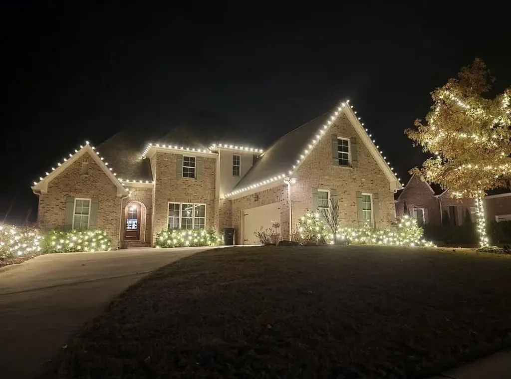 Warm white roofline Christmas lights on a brick two-story home at night.