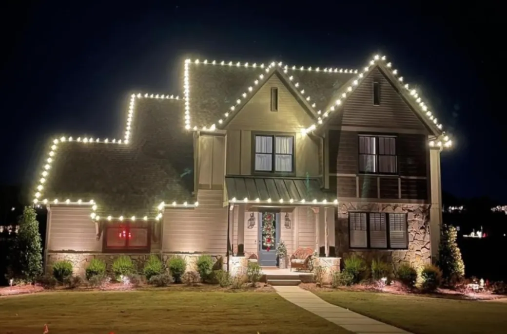 Warm white roofline lights on a craftsman-style home with landscape uplighting at night.