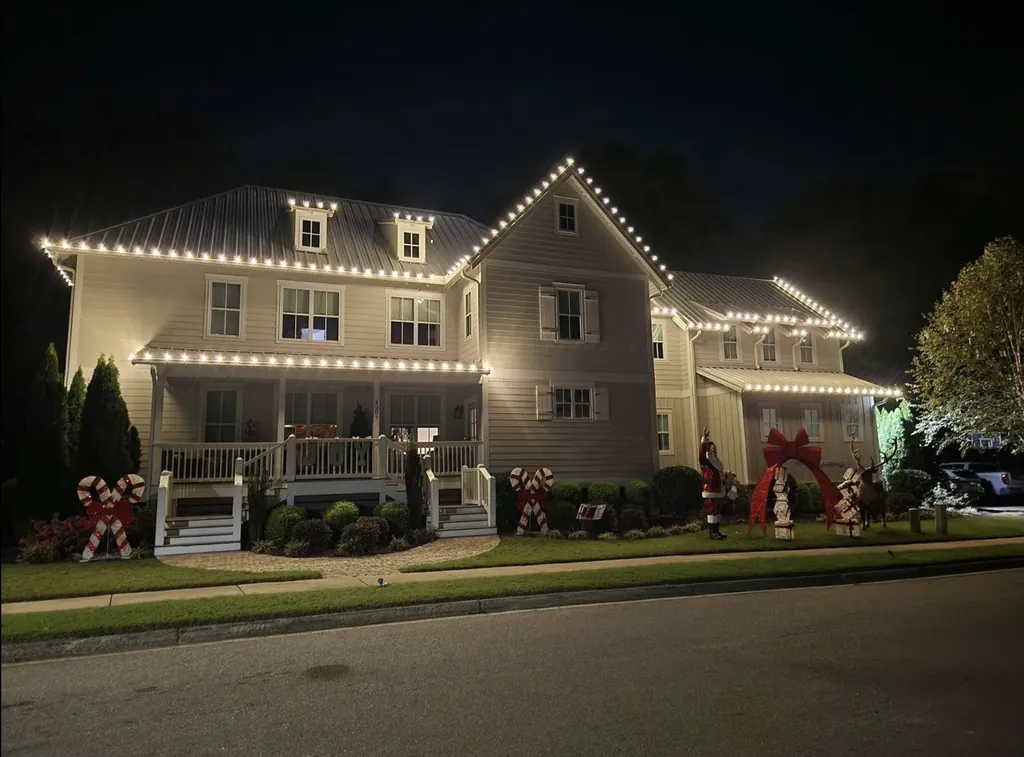 Warm white roofline lights outlining a two-story home with a wraparound porch.