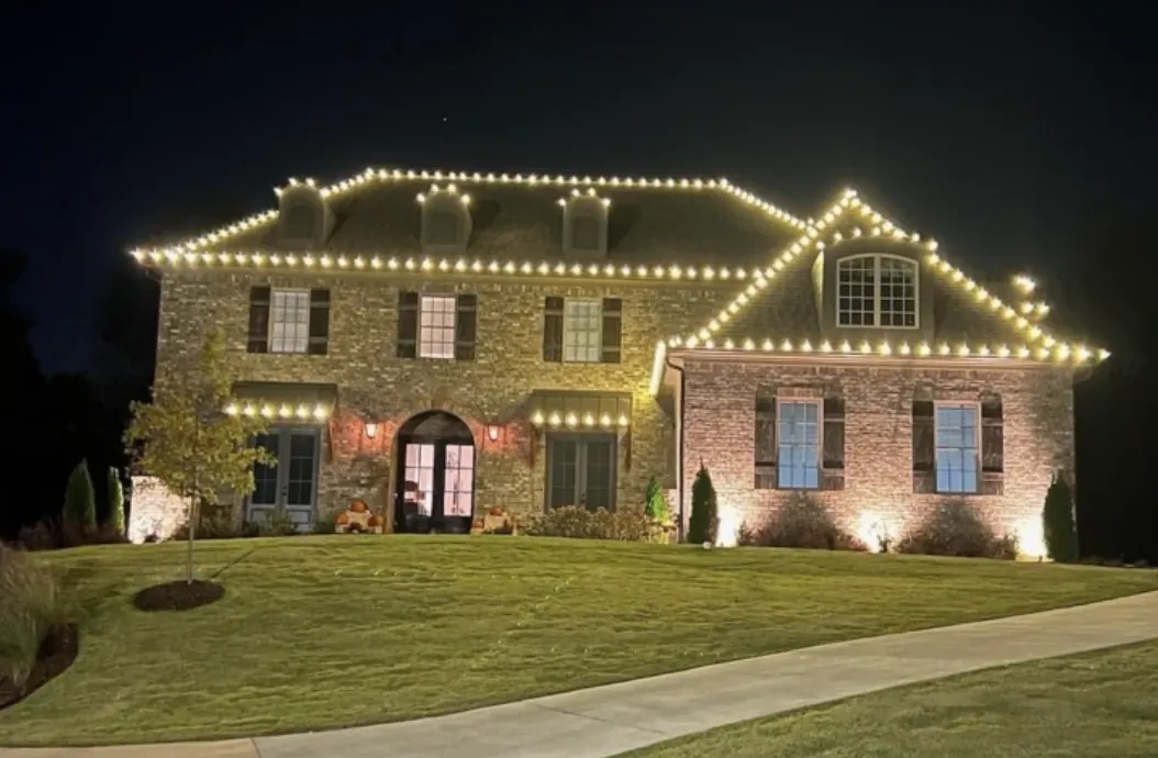 Roofline and dormer lights on a stone and brick two-story home above a front lawn.
