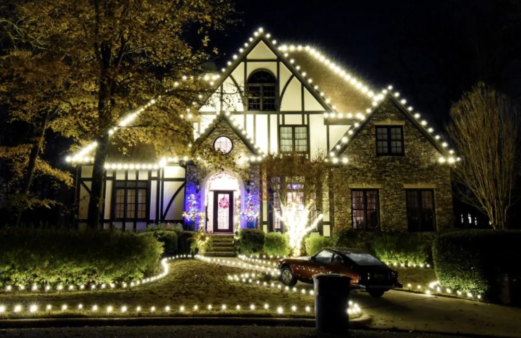 Roofline and walkway lights on a Tudor-style home with a tall arched dormer at night.